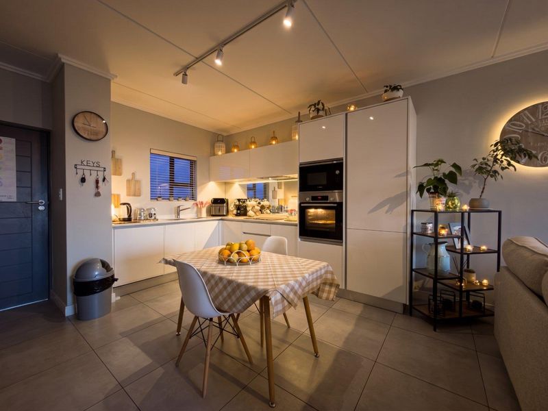 Modern open-plan kitchen featuring sleek white cabinetry, integrated appliances, mirrored splashback, and contemporary tiled flooring, creating a functional and well-lit living space.