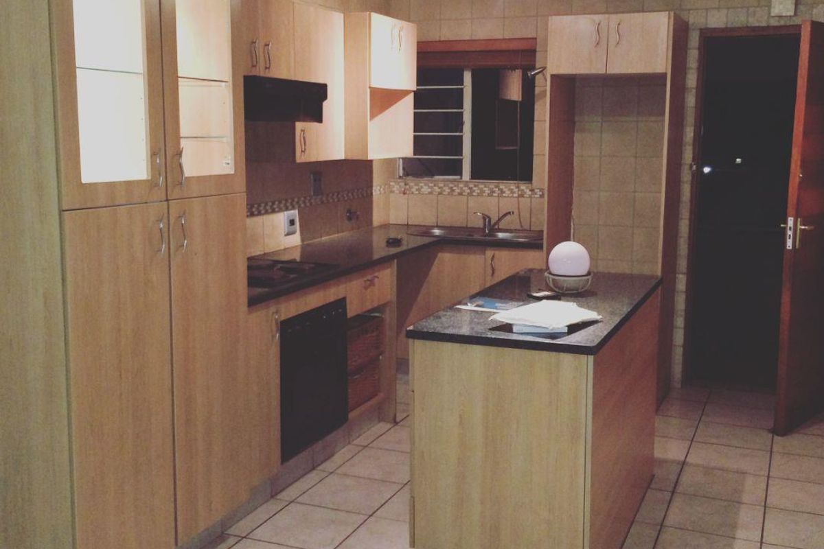 A functional kitchen featuring light wood-finish cabinetry, a central island, dark countertops, tiled flooring, and integrated lighting, offering a practical layout for daily use.