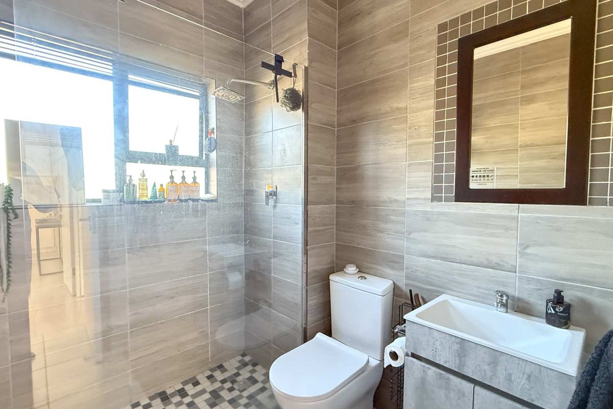 Modern bathroom featuring a glass-enclosed walk-in shower, wall-mounted vanity with basin, and neutral floor-to-ceiling tiling.