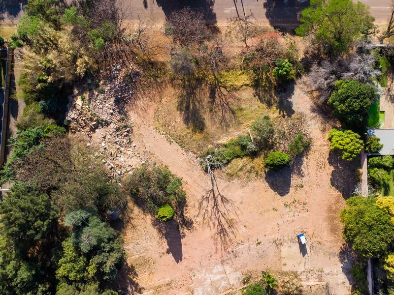 Aerial view of a vacant residential plot featuring mature trees and a cleared building site with some debris present.