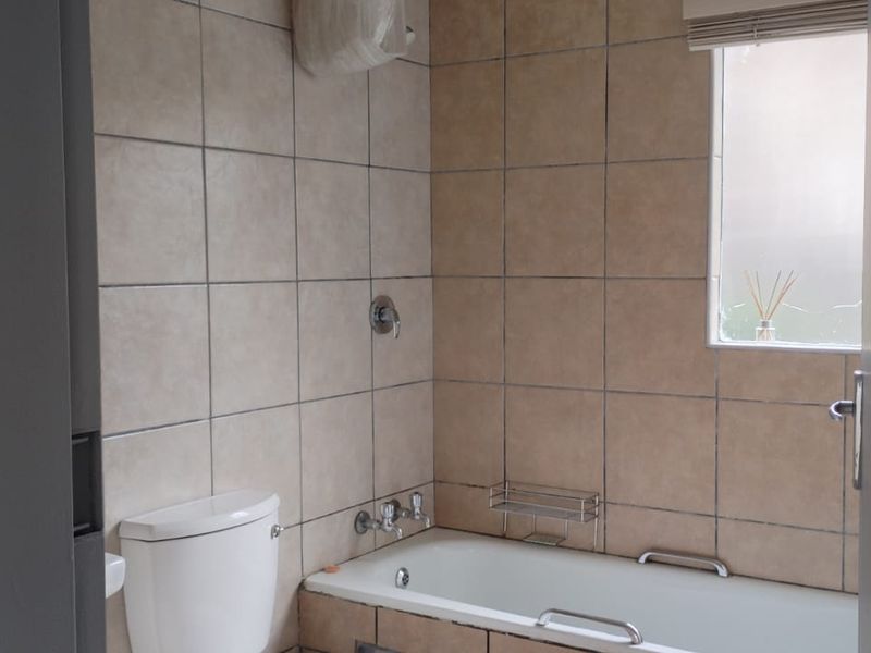 A functional bathroom featuring a bathtub with shower fixtures, a toilet, and neutral wall tiling, offering a clean and practical space.