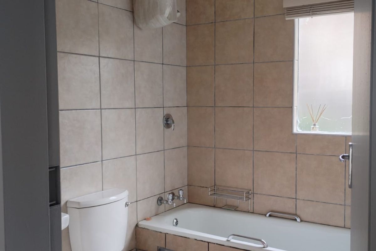 A functional bathroom featuring a bathtub with shower fixtures, a toilet, and neutral wall tiling, offering a clean and practical space.