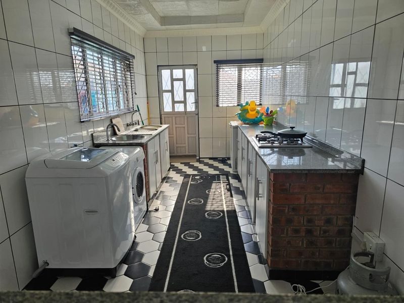 Functional scullery featuring tiled walls, granite countertops, built-in cabinetry, a gas hob, and a dedicated laundry area with sink.