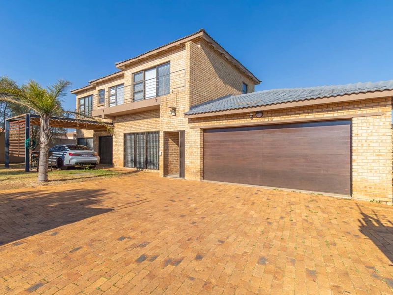 A double-story face brick house featuring a paved driveway, double garage, and an upper-level balcony with a pergola-covered side area.