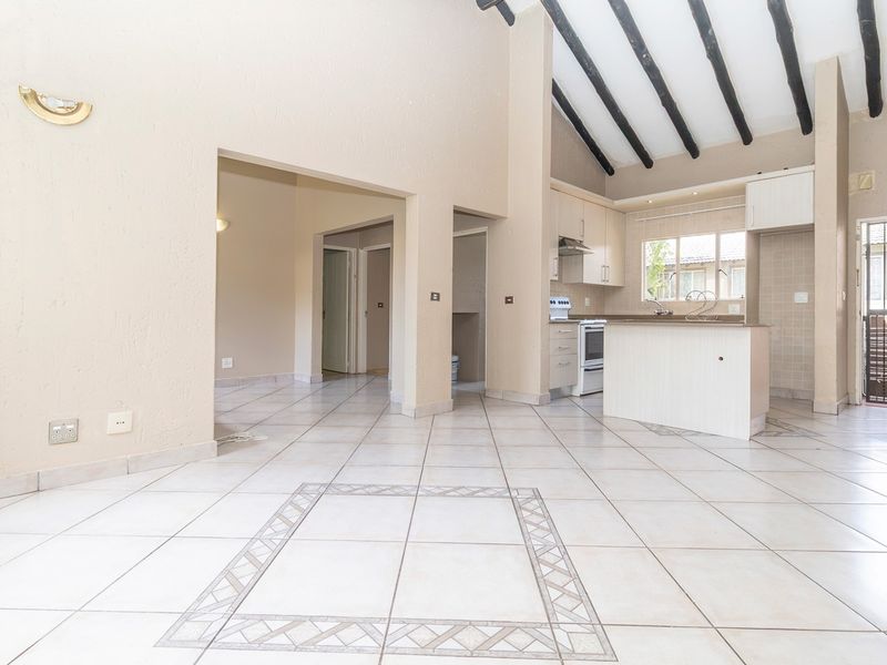Spacious open-plan living and kitchen area featuring high vaulted ceilings with exposed timber beams, tiled flooring, and a functional kitchen layout.