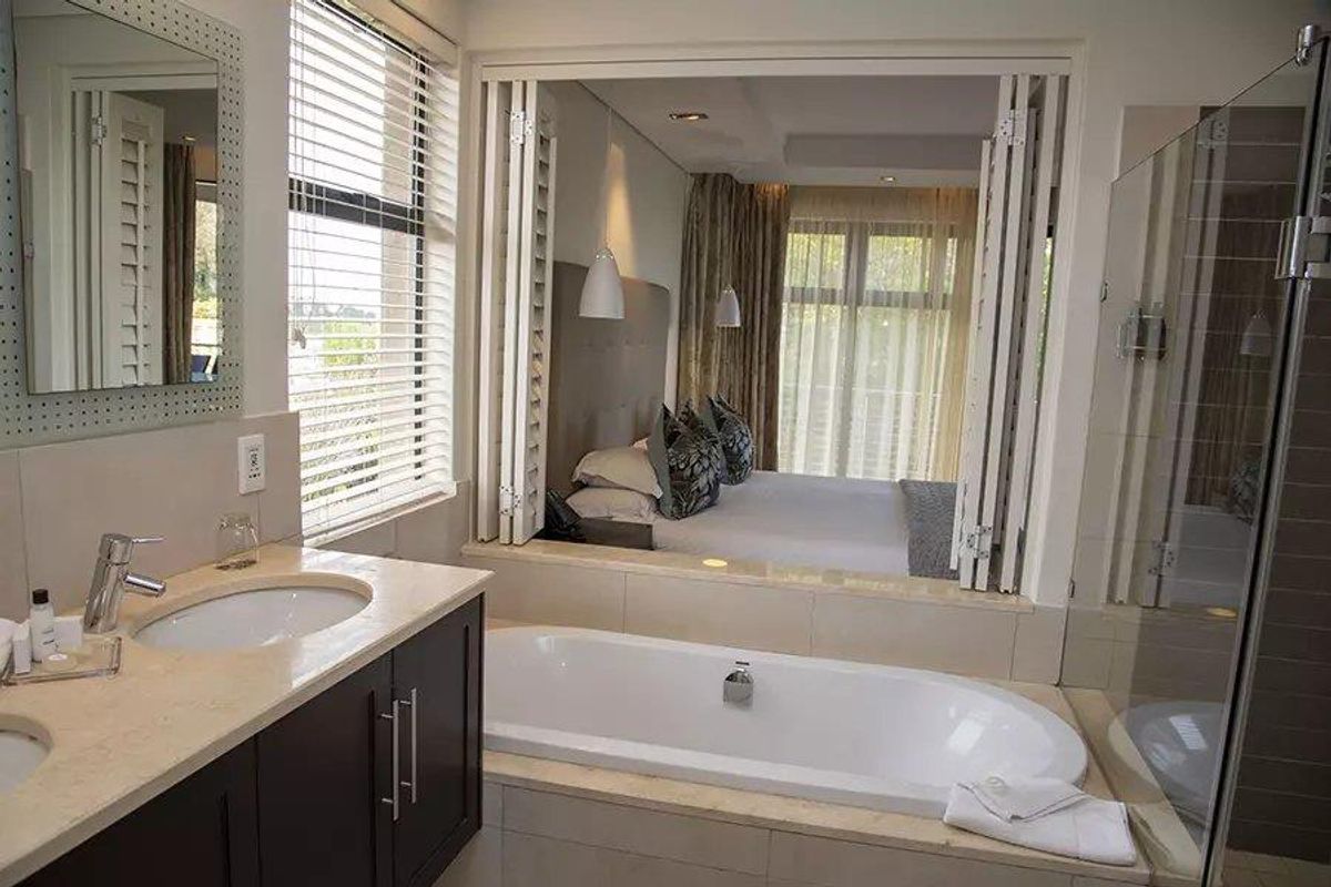 Modern en-suite bathroom featuring a built-in vanity, deep soaking tub, and glass-enclosed shower, with folding doors opening directly into the adjacent bedroom.