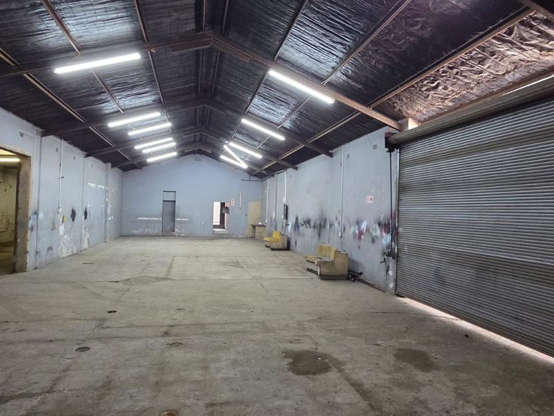 Spacious industrial utility area featuring high ceilings with exposed trusses, concrete flooring, and a large roller shutter door for easy access.