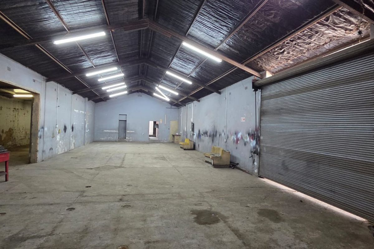 Spacious industrial utility area featuring high ceilings with exposed trusses, concrete flooring, and a large roller shutter door for easy access.