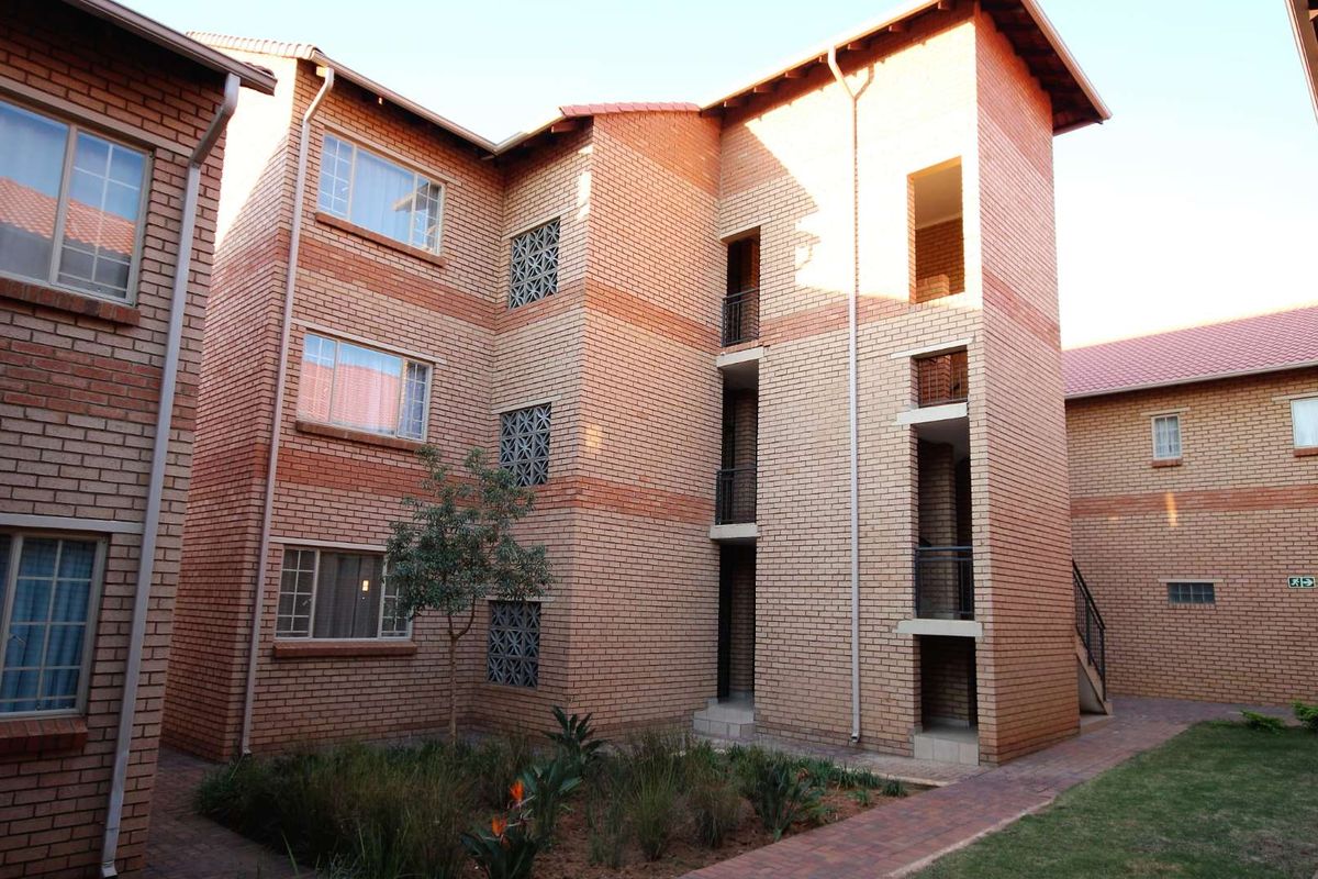 Exterior view of a multi-story apartment complex featuring face brick construction, tiled roofing, and a landscaped courtyard with paved walkways.