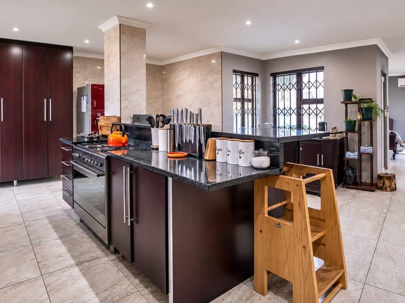 Spacious open-plan kitchen featuring dark wood cabinetry, granite countertops, and a gas stove, seamlessly flowing into the adjacent living area.