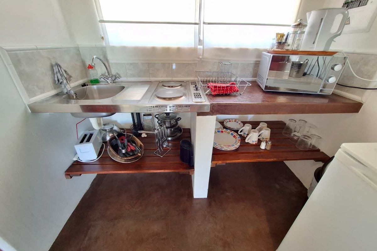 A compact kitchenette area featuring a stainless steel sink, integrated cooktop, and open wooden shelving for storage.
