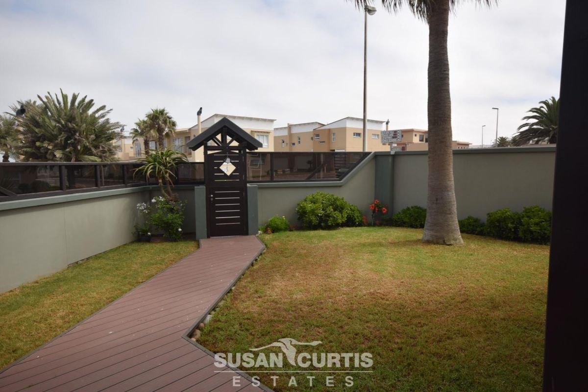 A private rear garden featuring a well-maintained lawn, a timber decking pathway, and a secure pedestrian gate set within a perimeter wall.