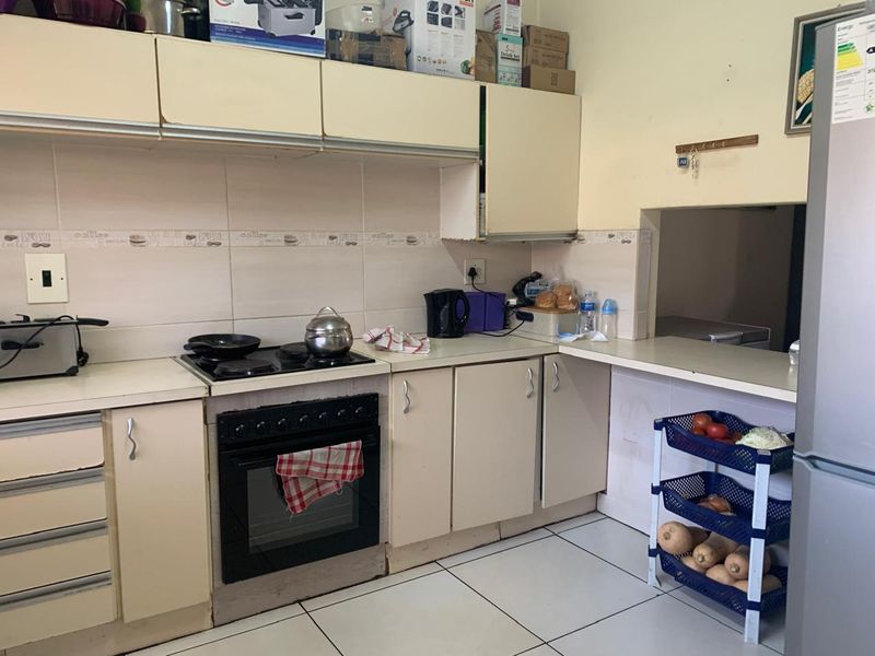 A functional kitchen featuring built-in cabinetry, an electric oven and hob, tiled backsplash, and a convenient pass-through window to the adjacent living area.