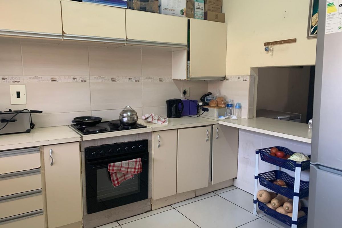 A functional kitchen featuring built-in cabinetry, an electric oven and hob, tiled backsplash, and a convenient pass-through window to the adjacent living area.