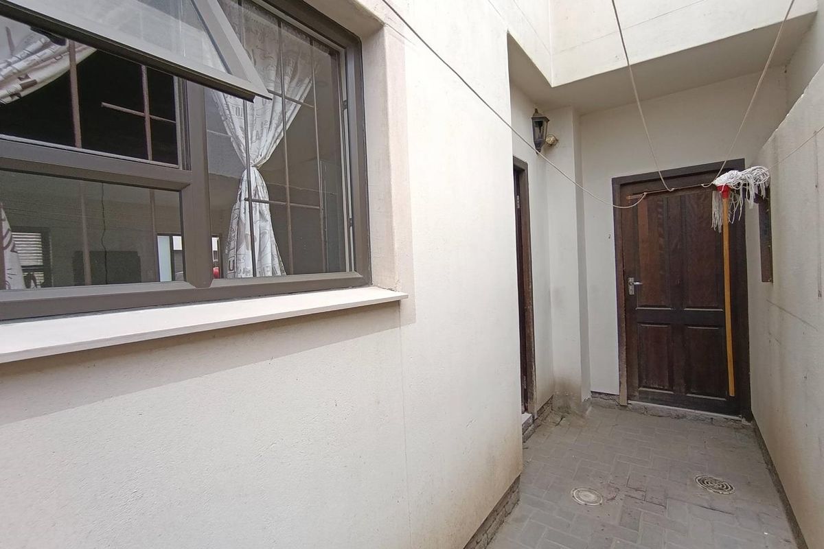 A narrow exterior side passage featuring paved flooring, a dark timber door, and an aluminium-framed window with security bars.