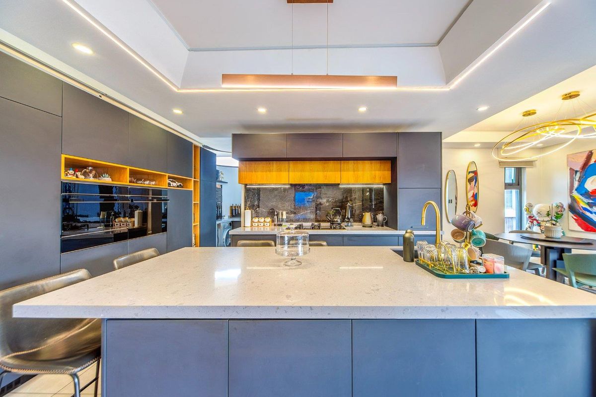 Modern kitchen featuring a large central island with stone countertops, sleek dark cabinetry, integrated appliances, and sophisticated recessed and pendant lighting.