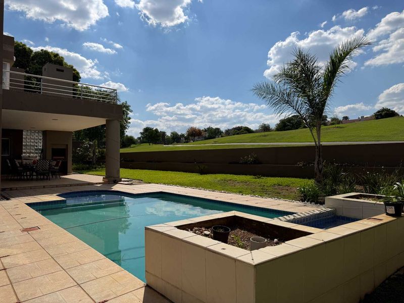 Outdoor pool area featuring a tiled patio, built-in braai, and a raised planter box, overlooking a landscaped garden and golf course view.