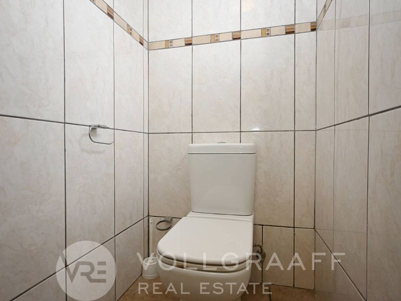 A compact guest bathroom featuring floor-to-ceiling ceramic wall tiles and a standard white toilet.