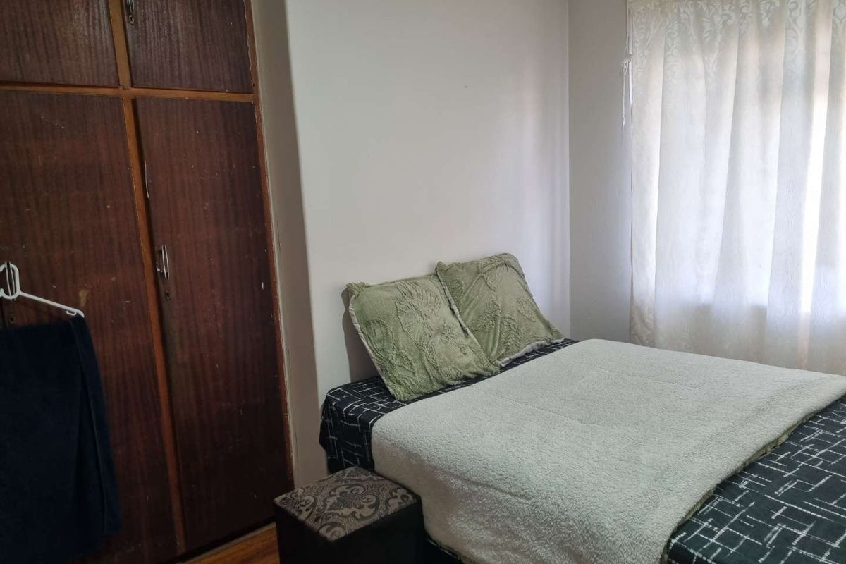 A functional bedroom featuring a built-in wooden wardrobe and natural light from the window.