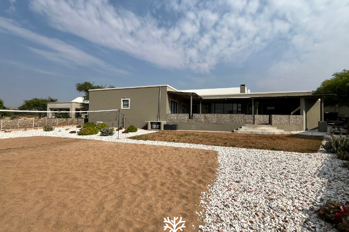 Rear view of the property featuring a covered patio, landscaped garden area with sand court, and stone-clad retaining walls.