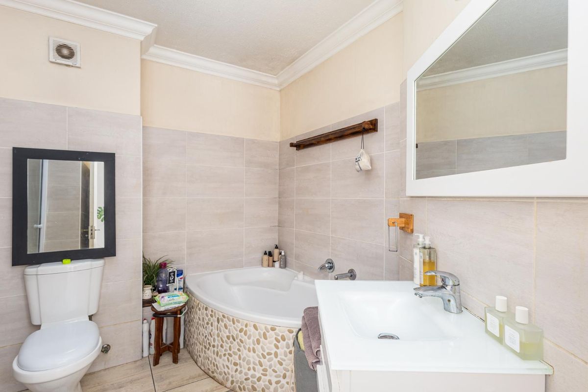 A well-maintained bathroom featuring a corner bathtub with decorative pebble tiling, a wall-mounted basin, and neutral wall tiles.