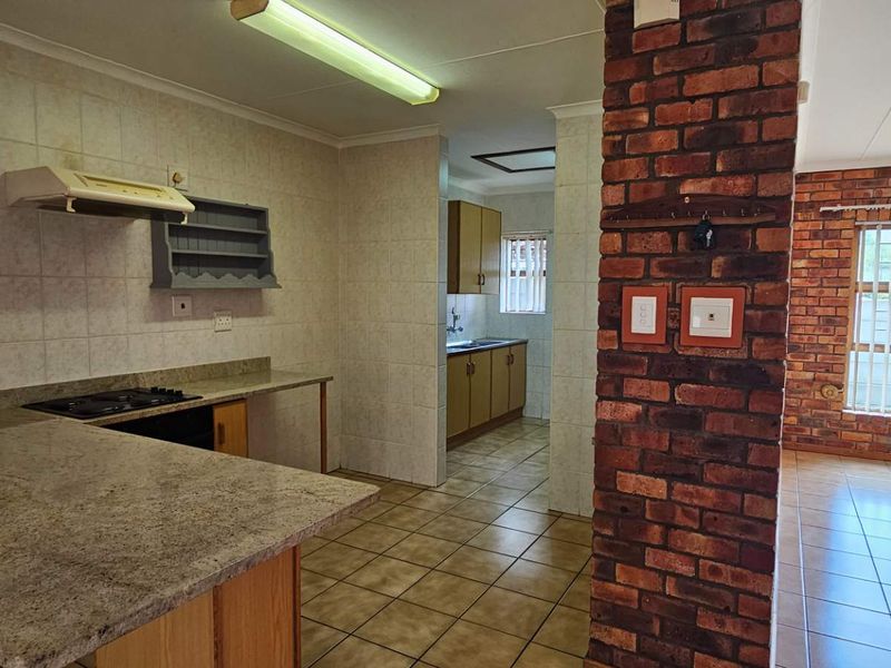 Open plan kitchen and living area featuring granite countertops, built-in hob, extractor fan, and distinctive exposed brick pillar with tiled flooring throughout.
