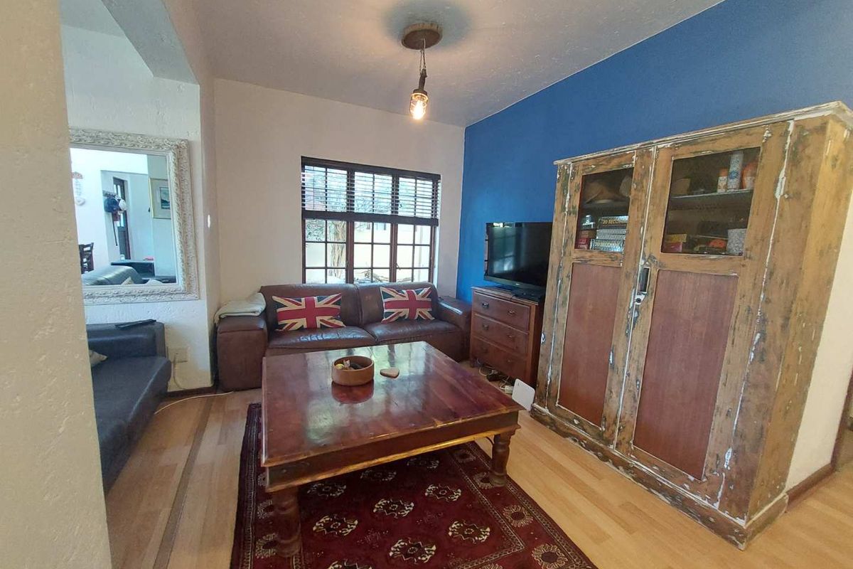 A living room featuring laminate flooring, a central pendant light, and a window with fitted blinds, offering a functional space for relaxation.