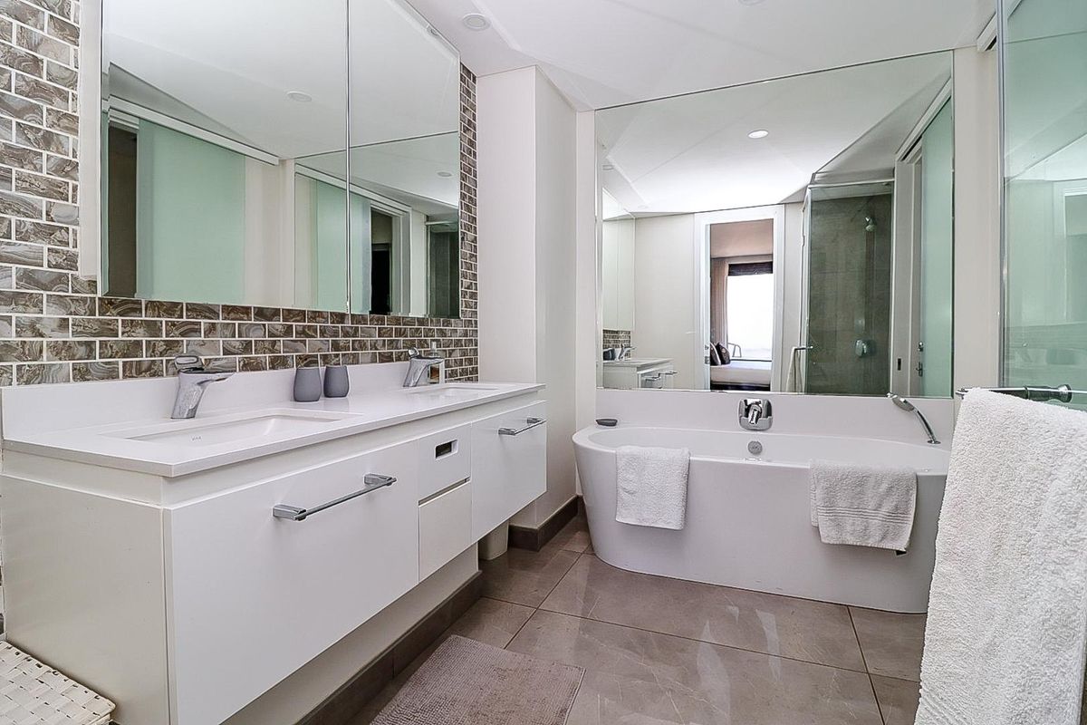 Modern bathroom featuring a double vanity, large wall mirror, mosaic tile backsplash, and a sleek freestanding bathtub with a separate glass shower enclosure.