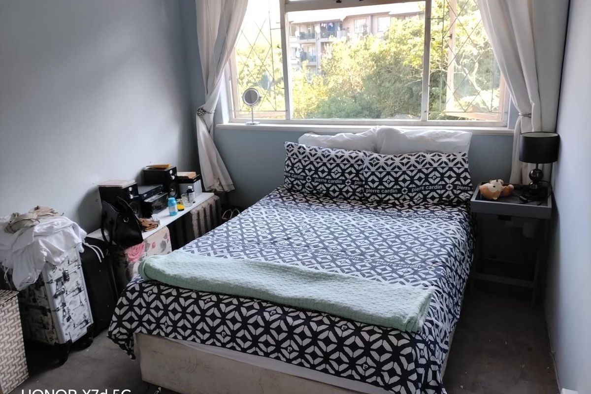 A compact bedroom featuring a large window with security bars, providing natural light and a view of the surrounding neighborhood.