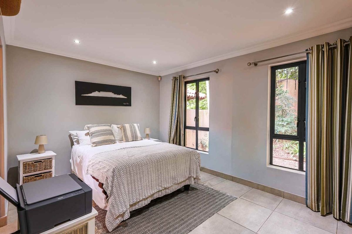 A well-lit bedroom featuring neutral wall tones, tiled flooring, and large windows that provide natural light and views of the garden.