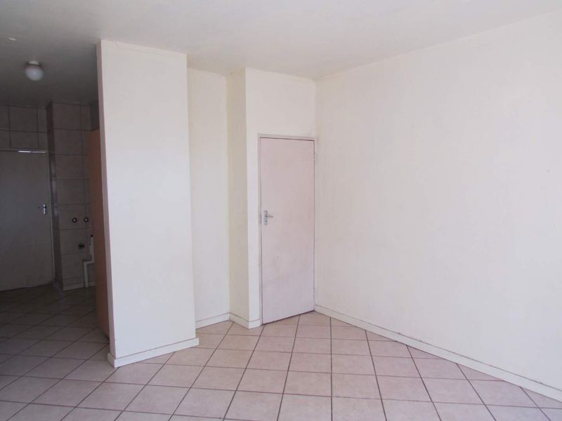 An empty living area featuring neutral tiled flooring and plain white walls, providing a blank canvas for interior design updates.