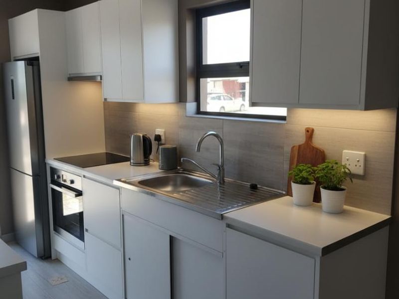 Modern kitchen featuring sleek white cabinetry, stainless steel sink, integrated oven and hob, and contemporary under-cabinet lighting.
