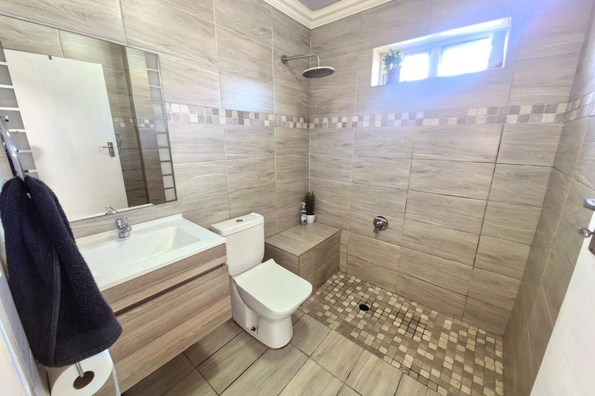 Modern bathroom featuring a walk-in shower with mosaic floor tiling, wall-mounted vanity, and neutral wood-look ceramic wall tiles.