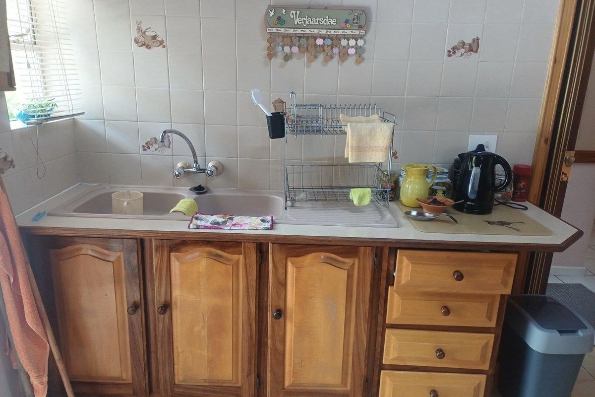 A functional kitchen sink area featuring wooden cabinetry, a double basin sink, and tiled backsplash.