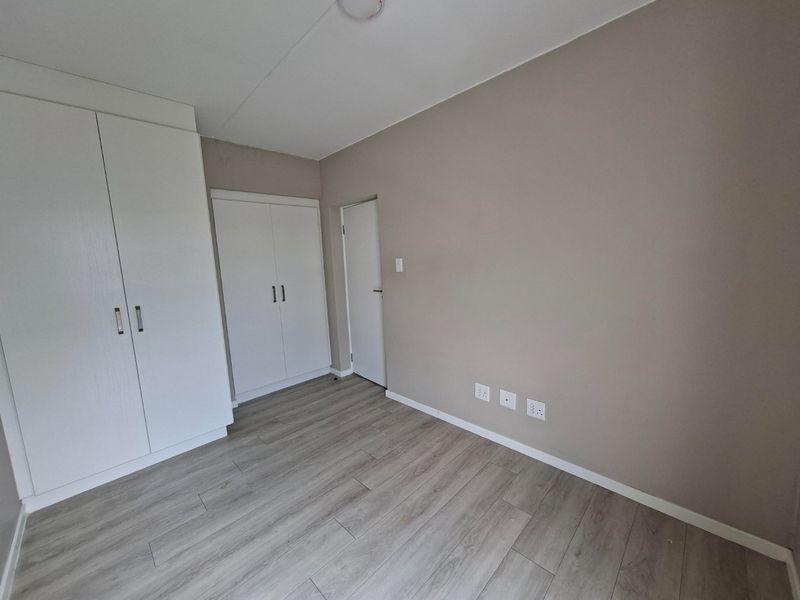 A clean, vacant bedroom featuring neutral wall tones, modern laminate flooring, and ample built-in cupboard storage.