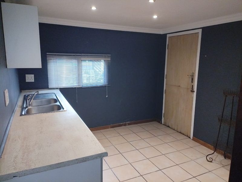 A functional kitchen area featuring a stainless steel double sink, laminate countertops, tiled flooring, and recessed lighting, ready for a modern update.