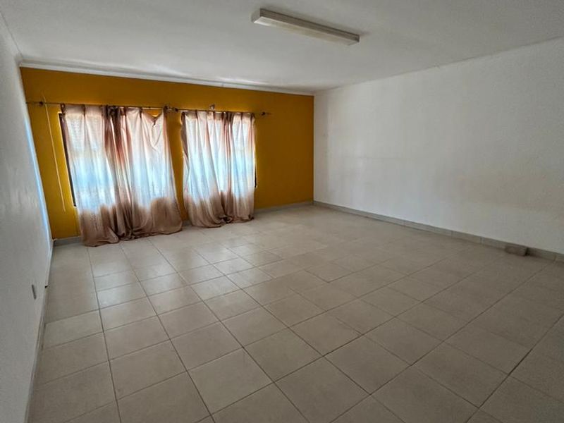 An empty living room featuring ceramic floor tiles, a fluorescent ceiling light, and a prominent mustard-colored accent wall.