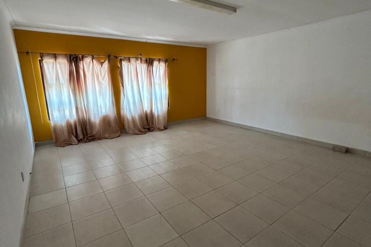 An empty living room featuring ceramic floor tiles, a fluorescent ceiling light, and a prominent mustard-colored accent wall.