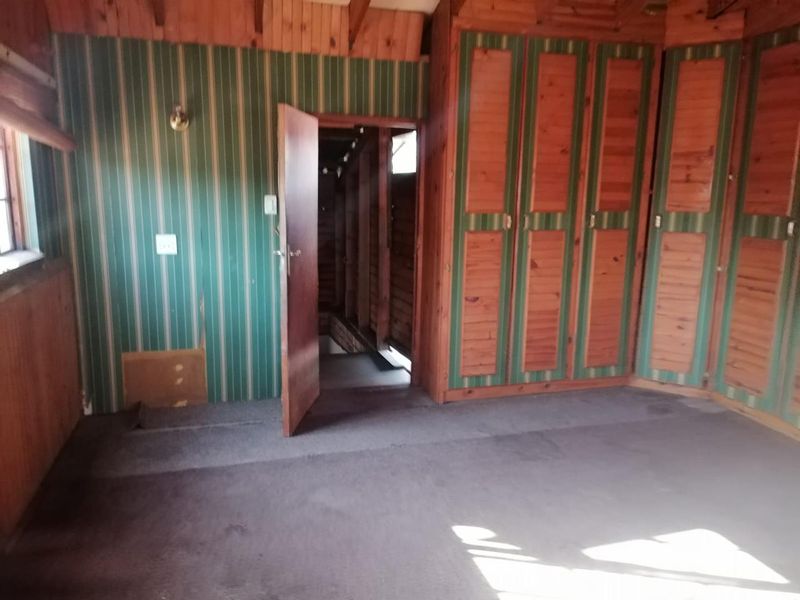 A vacant bedroom featuring built-in timber cupboards, striped wallpaper, and timber wall paneling, requiring cosmetic updates to modernize the space.