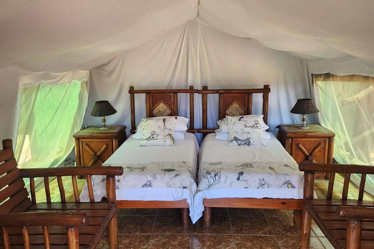 A rustic bedroom suite featuring twin beds with wooden headboards, tiled flooring, and a canvas tent-style ceiling structure.