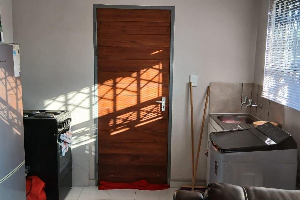 A functional kitchen area featuring a sink, tiled splashback, and space for major appliances, with a wooden door leading to the exterior.
