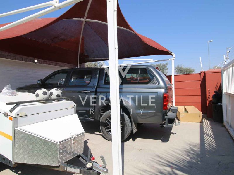 Outdoor parking area featuring a shade sail structure, concrete paving, and secure perimeter walling.