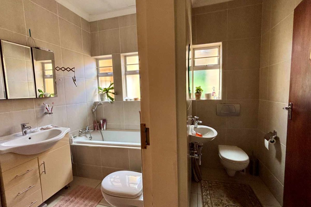 A functional bathroom featuring a bathtub, wall-mounted toilet, and vanity basin with neutral floor-to-ceiling tiling.