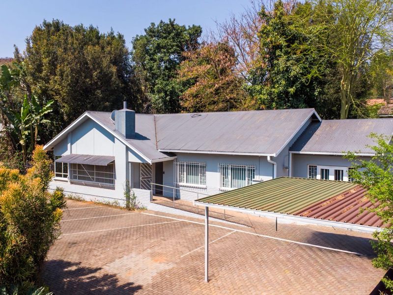 Front exterior view of a single-story house featuring a corrugated metal roof, paved driveway, and a detached carport structure.
