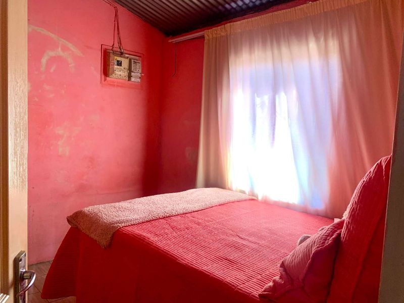 A bedroom featuring a corrugated metal ceiling and visible electrical distribution board, requiring significant cosmetic updates and wall repairs.