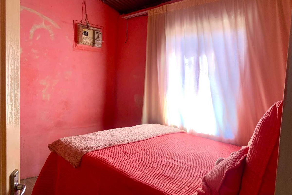 A bedroom featuring a corrugated metal ceiling and visible electrical distribution board, requiring significant cosmetic updates and wall repairs.