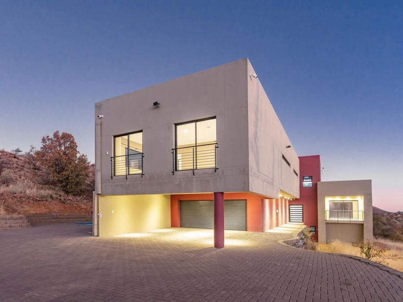 Modern multi-level residence featuring a paved driveway, double garage, and balconies, set against a natural hillside backdrop at dusk.