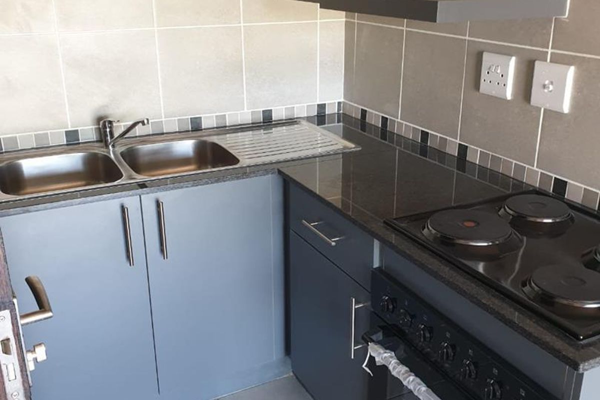 A compact, modern kitchen featuring grey cabinetry, granite countertops, a built-in oven with electric hob, and a double bowl stainless steel sink.
