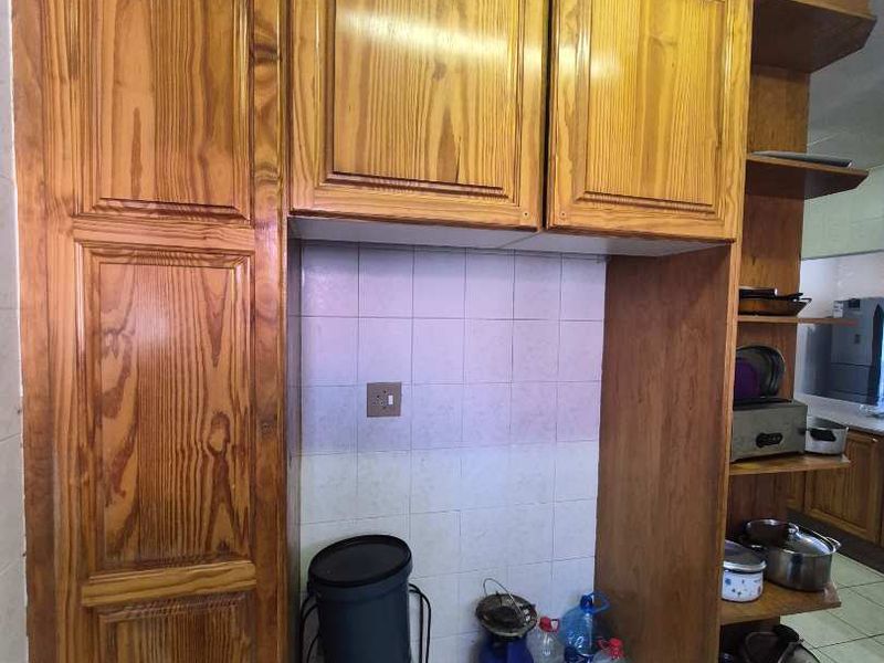 A kitchen area featuring dated wooden cabinetry, tiled backsplash, and tiled flooring with open shelving for storage.