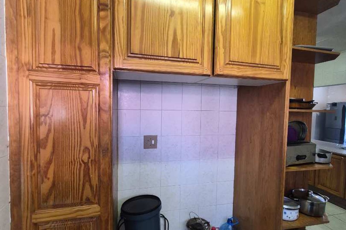 A kitchen area featuring dated wooden cabinetry, tiled backsplash, and tiled flooring with open shelving for storage.